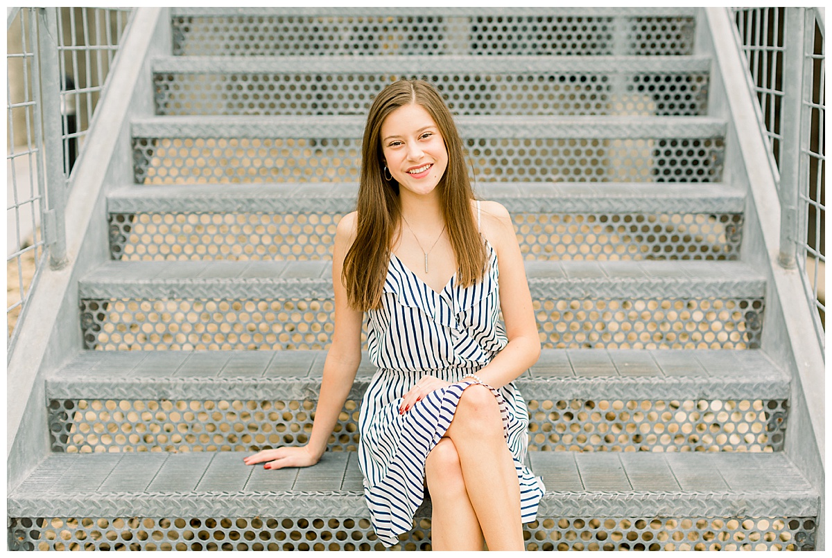 Girl smiling in striped dress sitting on metal steps.