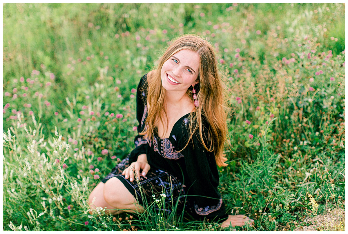 Girl kneeling in a field and smiling up at the camera.