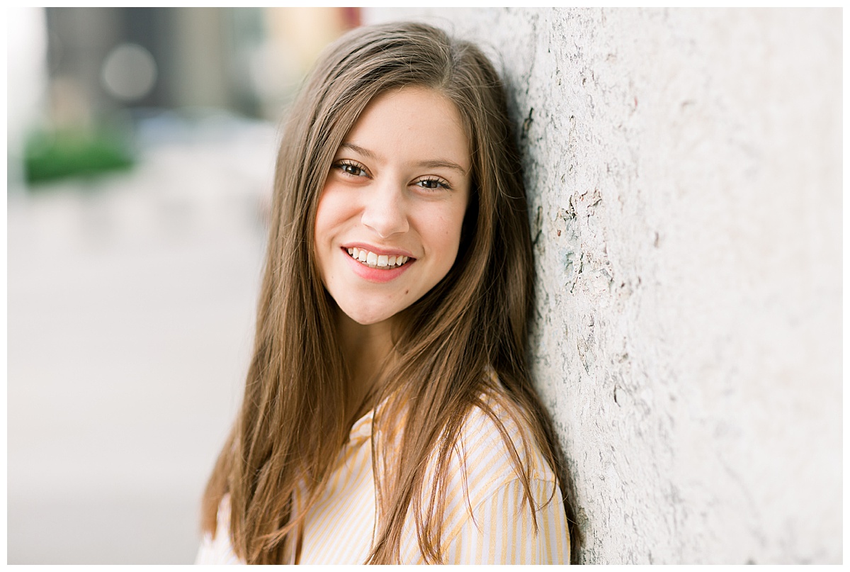 Girl leaning against a wall and smiling for senior pictures at Stone Arch Bridge.