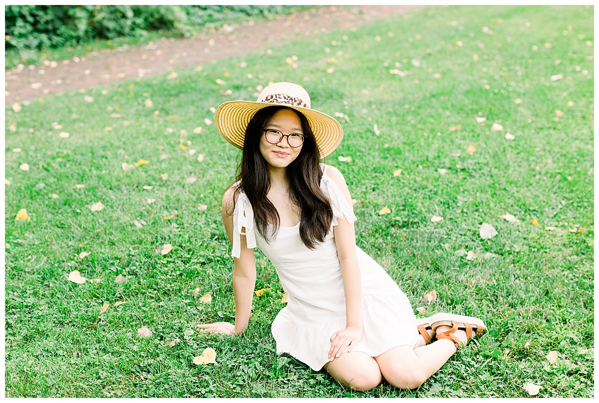 Girl wearing a hat and a white dress lounging in the grass in a Minneapolis park.