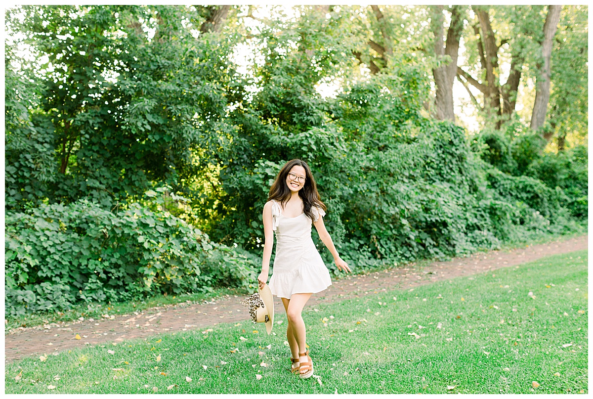 Girl in a white dress holding a hat skipping in the grass.