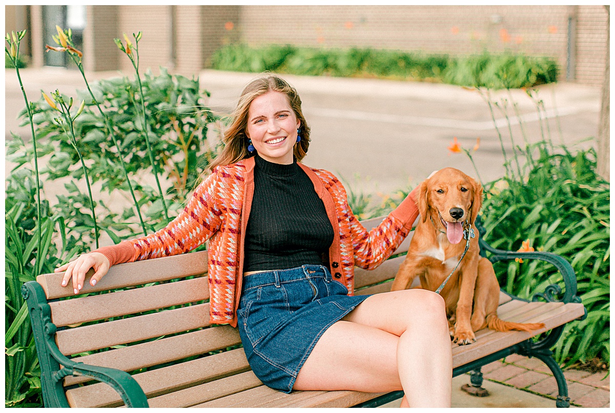 Girl sitting on a bench smiling and petting her dog.