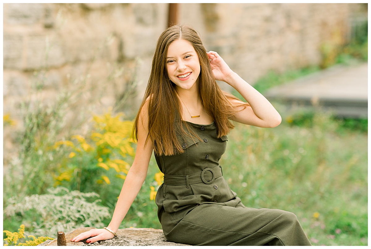 Girl sitting on a rock in a field with flowers for senior pictures at Stone Arch Bridge.