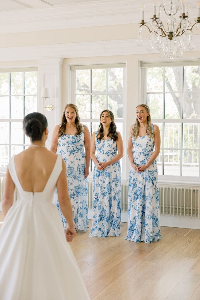 Bridesmaids in blue and white floral dresses react with joy to seeing the bride at The Minikahda Club