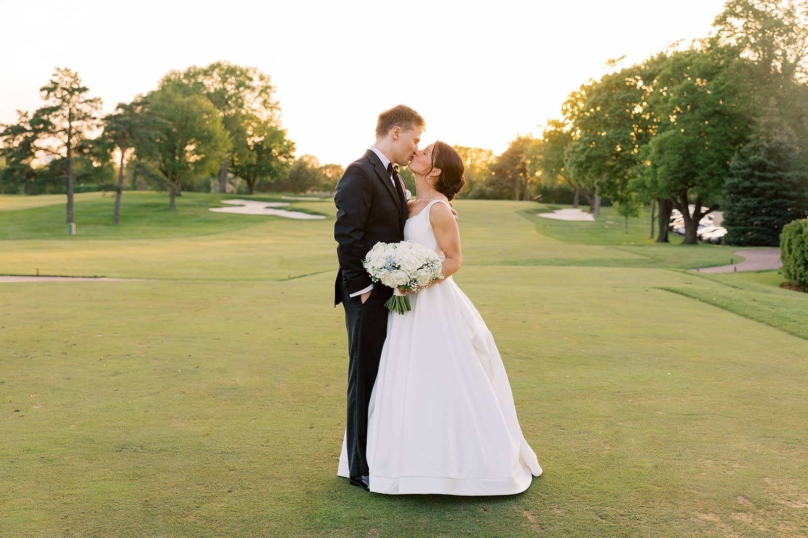 Classic wedding portrait of bride and groom kissing at sunset with a white and blue rose bouquet