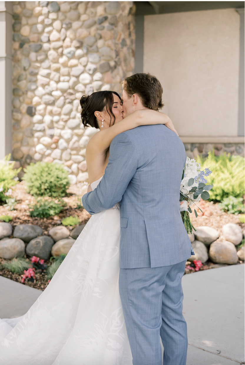 Bride and groom embracing for the first time in front of the stone exterior and summer garden at their Minnesota wedding venue