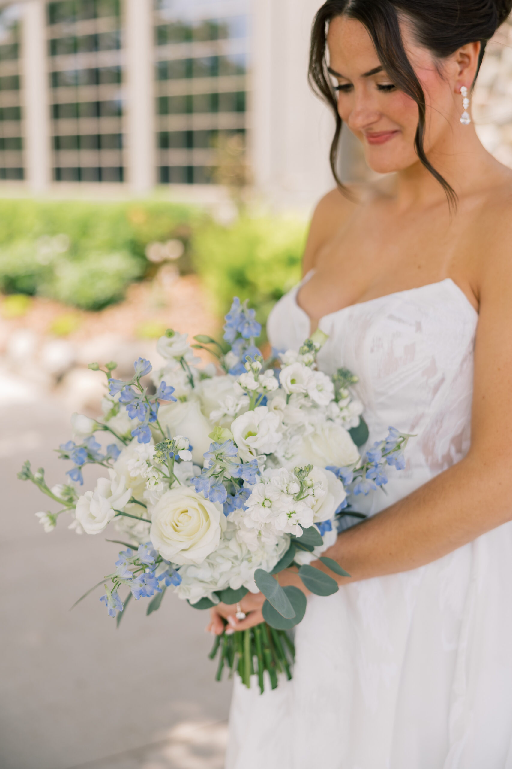 Close-up of bride holding a lush white rose, lisianthus, sweet pea, and blue delphinium bridal bouquet at her Minnesota summer wedding